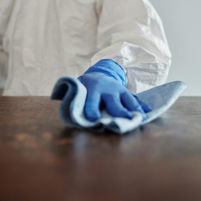 Person in protective suit using disinfectant on surface to ensure cleanliness and safety.